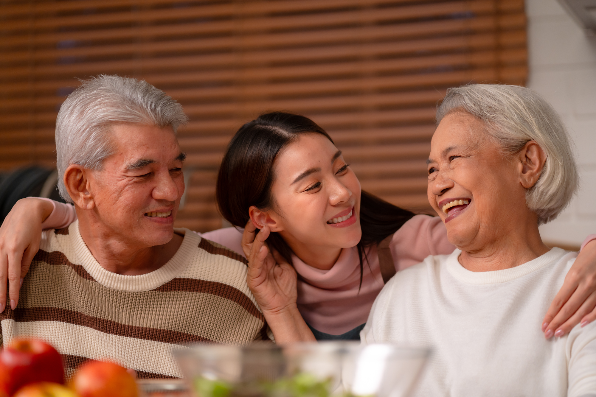 a young asian woman with her arms around her grandparents, as they smile looking at each other